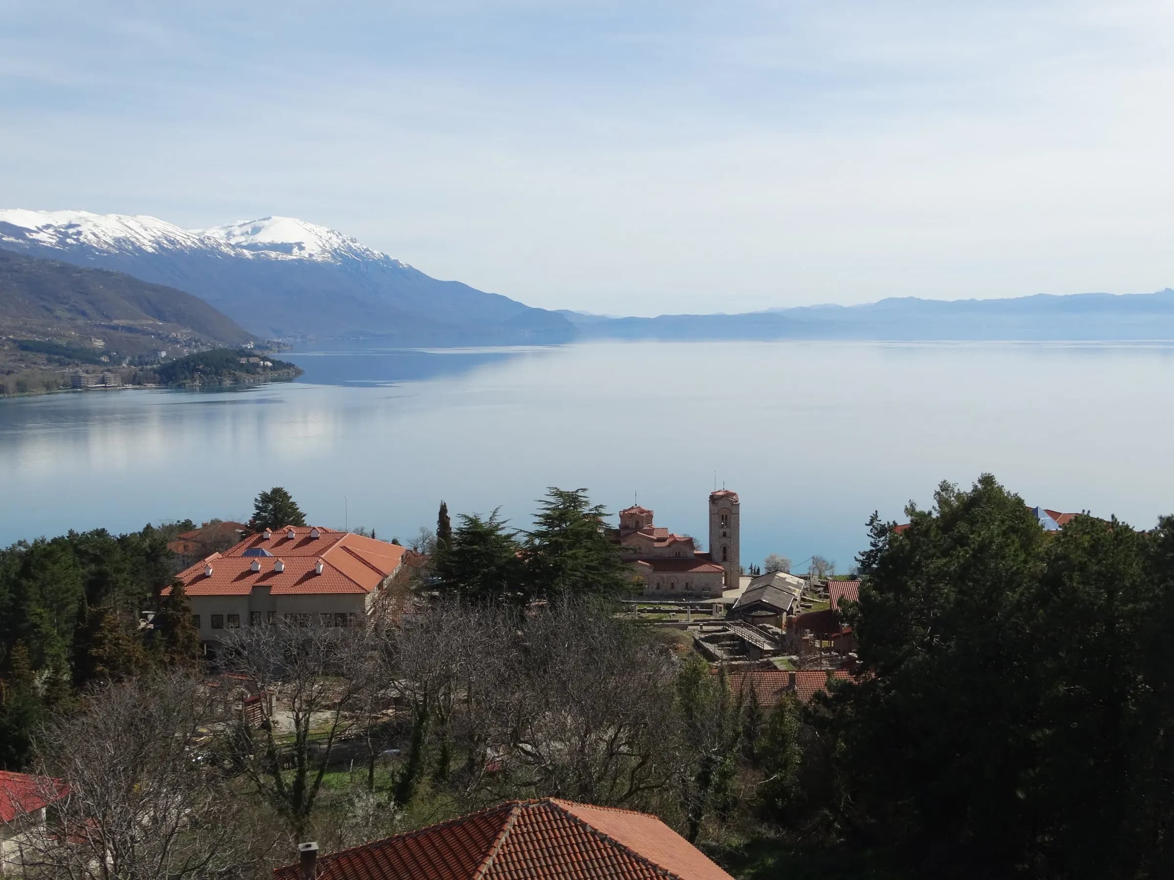 Lake Ohrid with snow-capped mountains beyond and the rooftops of Ohrid in the foreground.