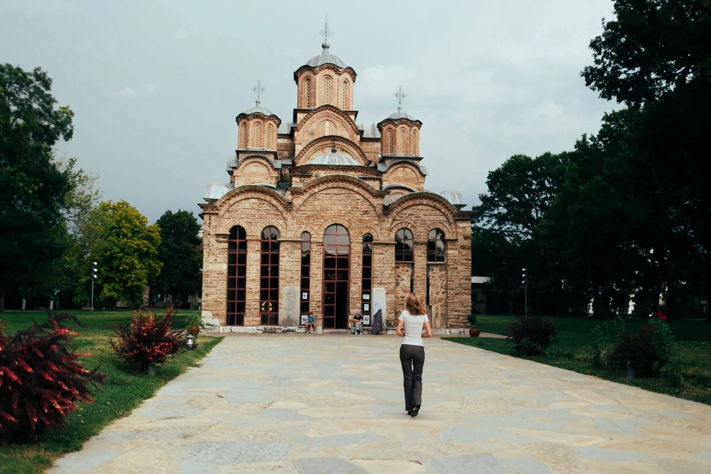 The church of Gračanica Monastery at the end of a stone path, with a visitor walking toward it.