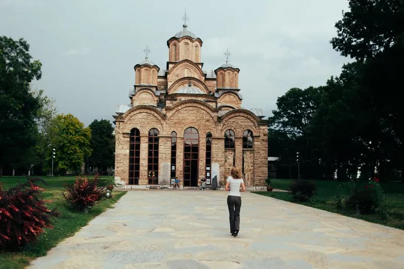 The church of Gračanica Monastery at the end of a stone path, with a visitor walking toward it.